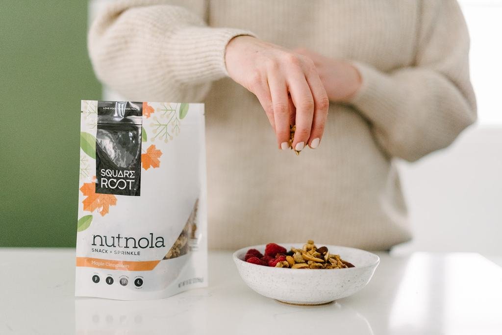 sprinkling square root nutnola on a bowl of yogurt and fruit